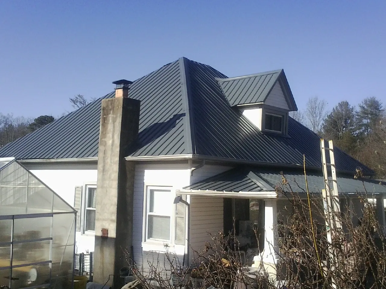 Dark blue standing seam metal roof on a white farmhouse with dormer — Slate & Tile Roof Repair by Roofing Brothers in Rocky River