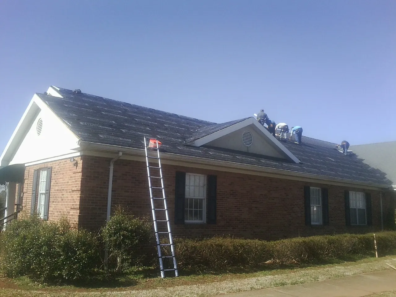 Crew tearing shingles off a brick ranch roof with a ladder set — Emergency Roof Repair work by our crew in Rocky River
