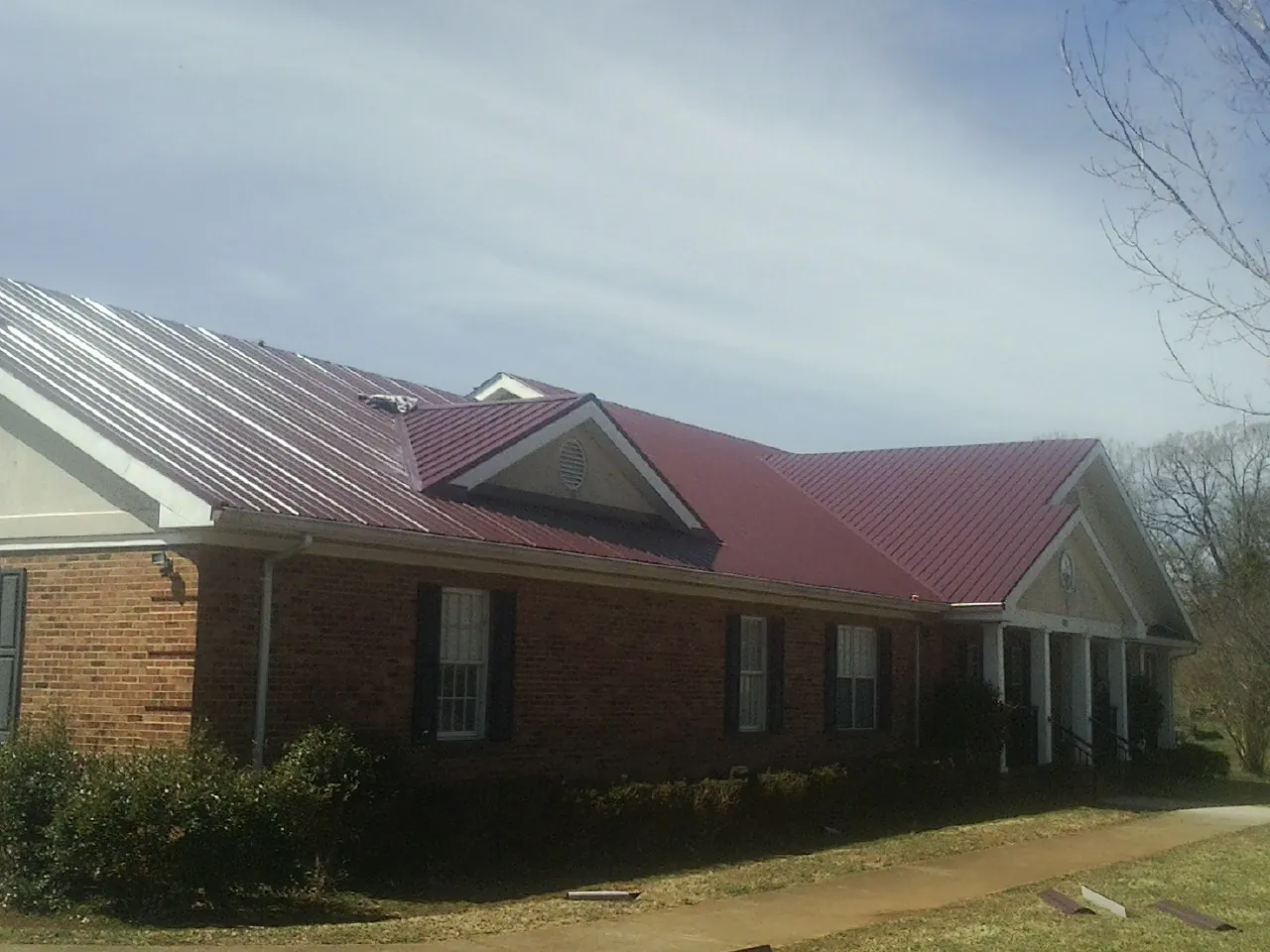 Red metal roof with gabled entries on a long brick building, from a Hail Damage Roof Repair job in Rocky River