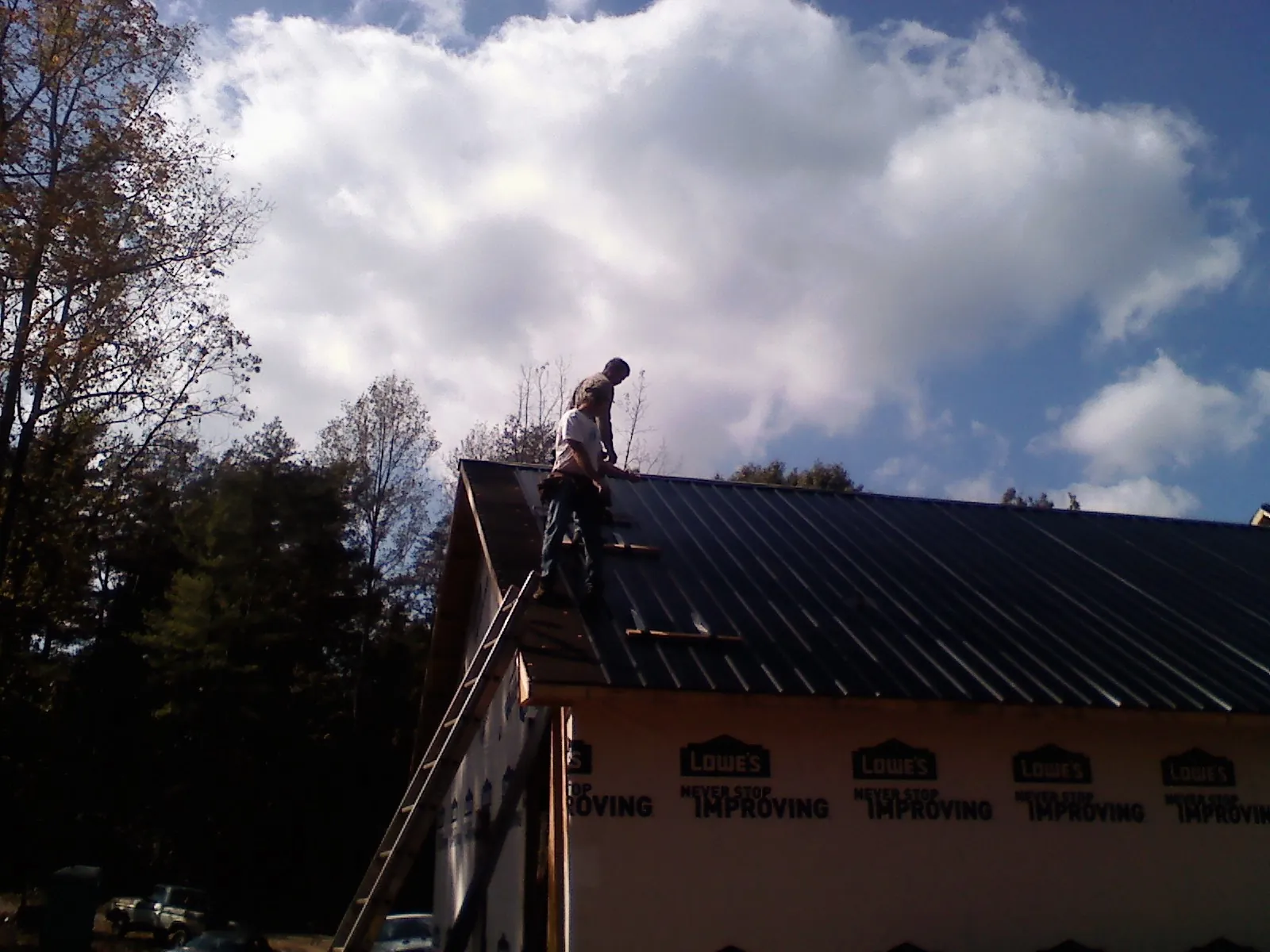 Roofer fastening dark metal panels high against a cloudy sky, from a Roof Inspection job in Rocky River
