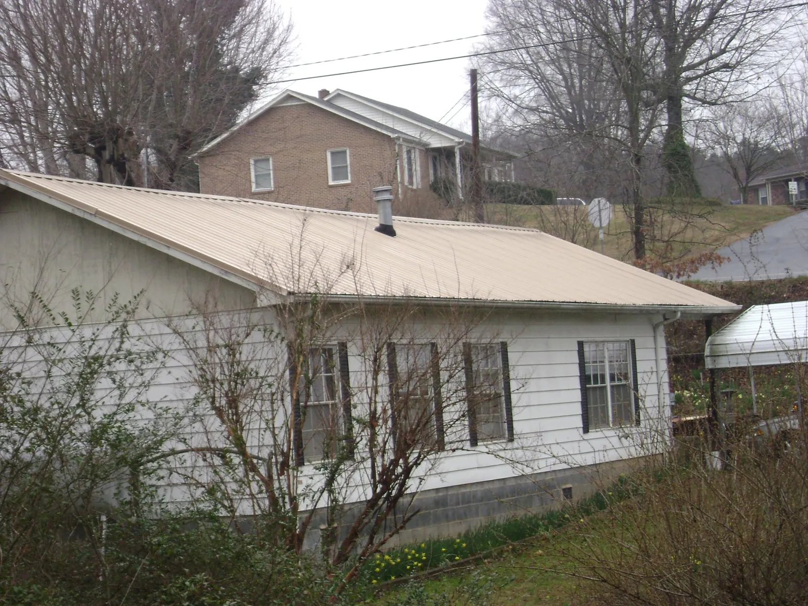 Tan metal roof on a white sided house set into a hillside — Commercial Roofing by Roofing Brothers in Rocky River